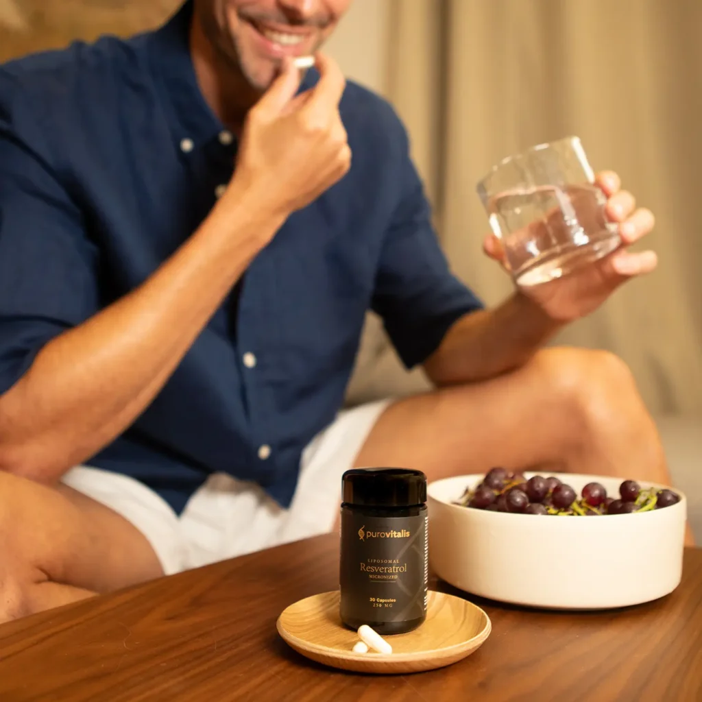 Supplement met liposomaal gemicroniseerd resveratrol. Afbeelding waarop een man een capsule inneemt naast druiven en een fles Purovitalis