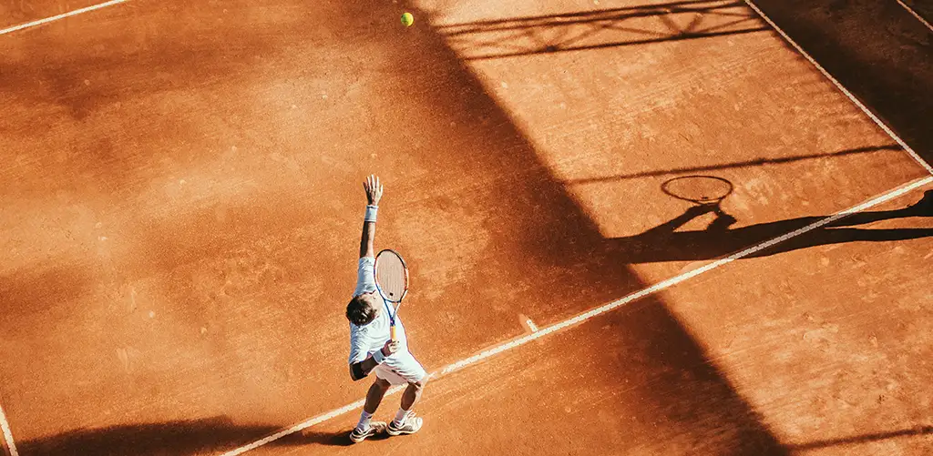 Man is playng tennins, tennis ball in the air ready to serve. High sun exposure. Bird's-eye view