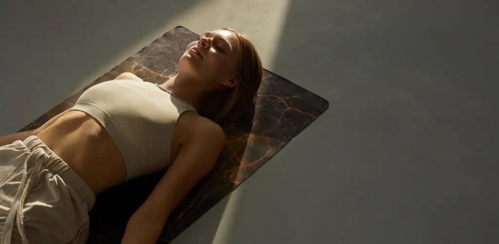 Una donna sdraiata tranquillamente su un tappetino da yoga sotto una luce soffusa, che si rilassa o medita durante una routine di benessere rilassante.