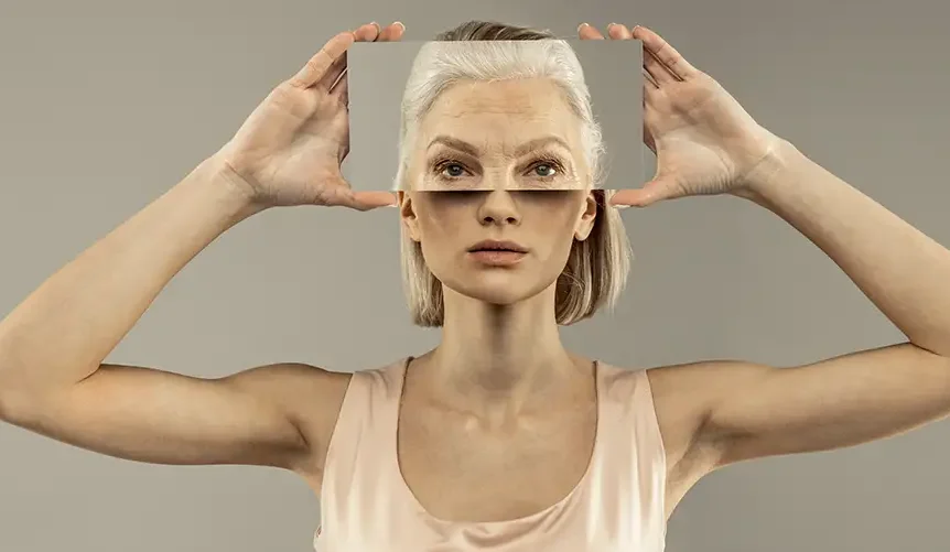 A woman holding a transparent panel in front of her face that shows an older version of her features, illustrating the contrast between youth and aging.