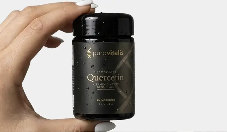 O mână care ține o sticlă neagră de Purovitalis cu eticheta “Quercetină lipozomală cu vitamina C, zinc și bromelaină”, pe care se pot vedea 30 de capsule, pe un fundal deschis.