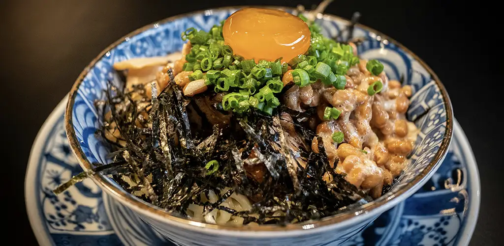 En skål natto toppet med rå æggeblomme, hakkede forårsløg og strimlet tang, serveret med ris.