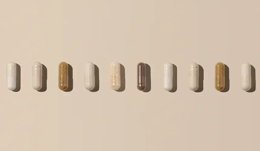 A row of different supplement capsules arranged in a straight line on a soft beige background, representing longevity and wellness supplements.